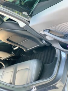 The image shows the interior of the backseat area of a vehicle. The seats are made of leather and appear clean and well-maintained. The car door is open, and parts of the door panel and front seatback are visible. The floor has dark, striped carpeting.