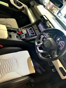 Interior of a luxury car featuring a sleek, modern design. The dashboard has a digital display, large central touchscreen, and various controls. The seats have a two-tone pattern with hexagonal stitching. The steering wheel displays multiple controls and the brand logo.